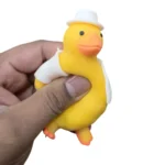 Cute Duck Squishy Toy featuring a yellow duck with an orange beak, brown floppy details, blue hat and blue outfit, individual packaging and wholesale display box, 10 × 6cm, £2.85 each – SDMAX Toys Wholesaler.
