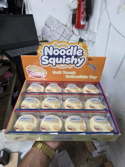 Cream-coloured Noodle Squishy Toy with a raised noodle-style texture, approximately 7 × 7 cm, shown in a 12-piece retail display box from SDMAX Toys Wholesaler.